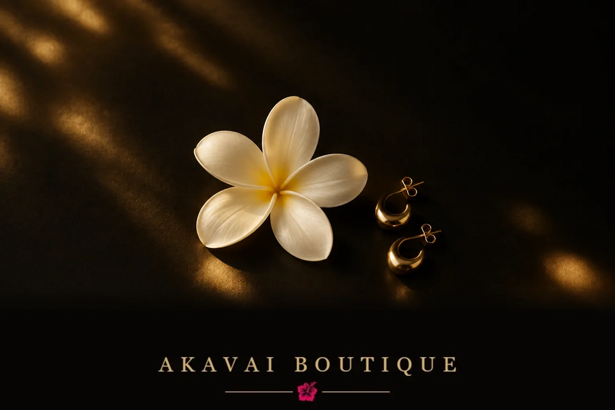 Fleur de frangipanier blanche et boucles d'oreilles dorées sur fond noir, lumière dorée tamisée, Akavai Boutique